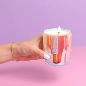 Colorful CBD-infused luxury candle held against a pastel backdrop, exuding elegance.