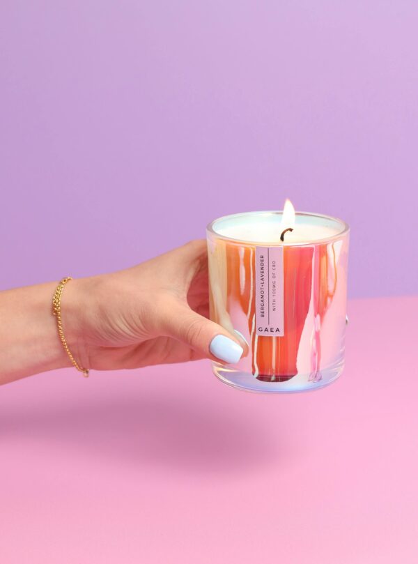 Colorful CBD-infused luxury candle held against a pastel backdrop, exuding elegance.